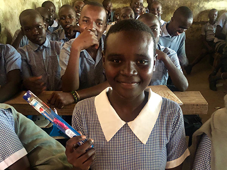 A female student holds up a packaged toothbrush with the rest of the class visible behind her